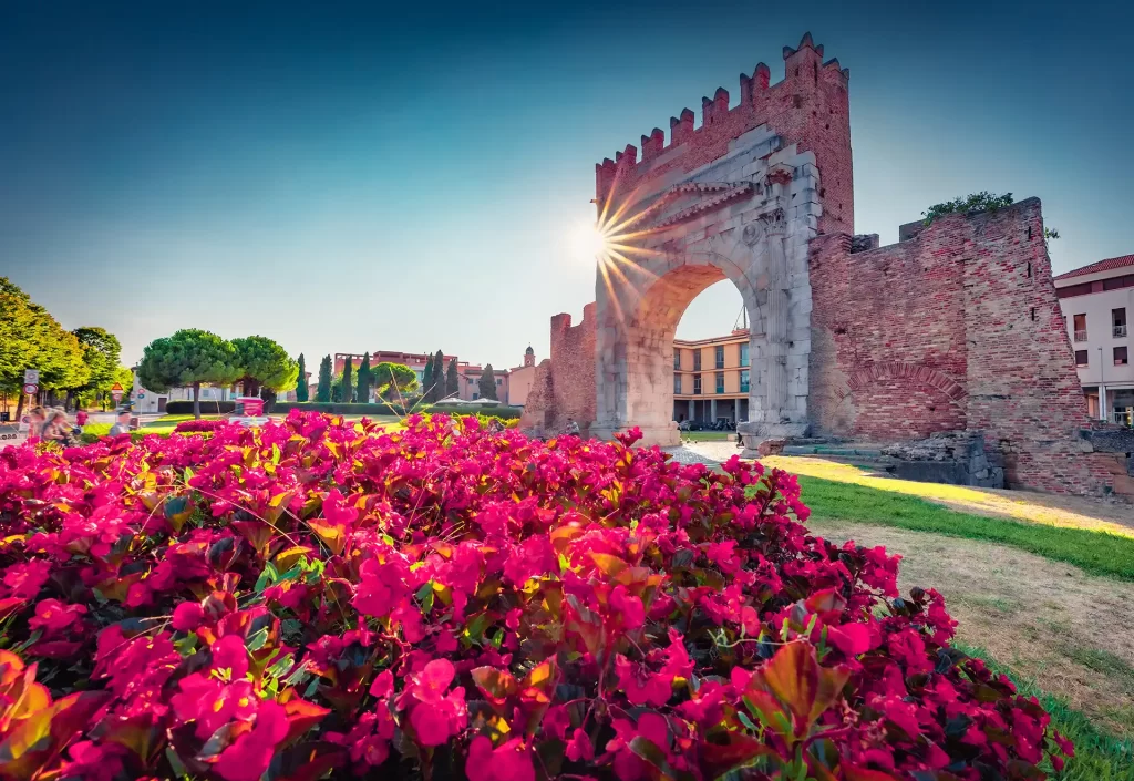 Arco storico tra fiori rosa al tramonto.
