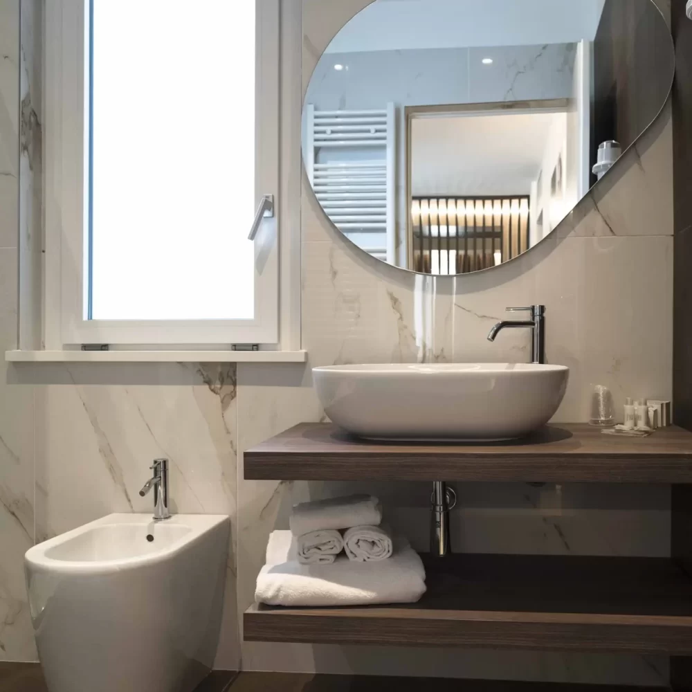 Bagno moderno con specchio rotondo, lavandino e bidet.