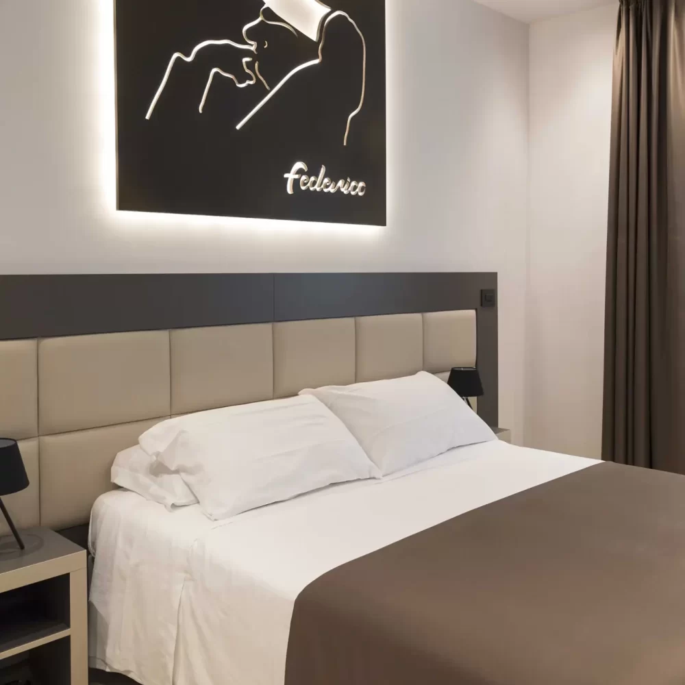 Camera da letto moderna con quadro illuminato raffigurante un volto con cappello.