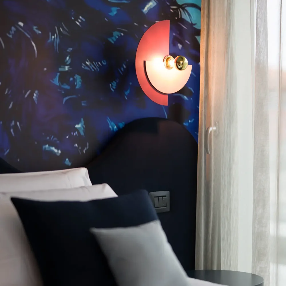 Letto moderno con cuscini decorativi e lampada a parete artistica.