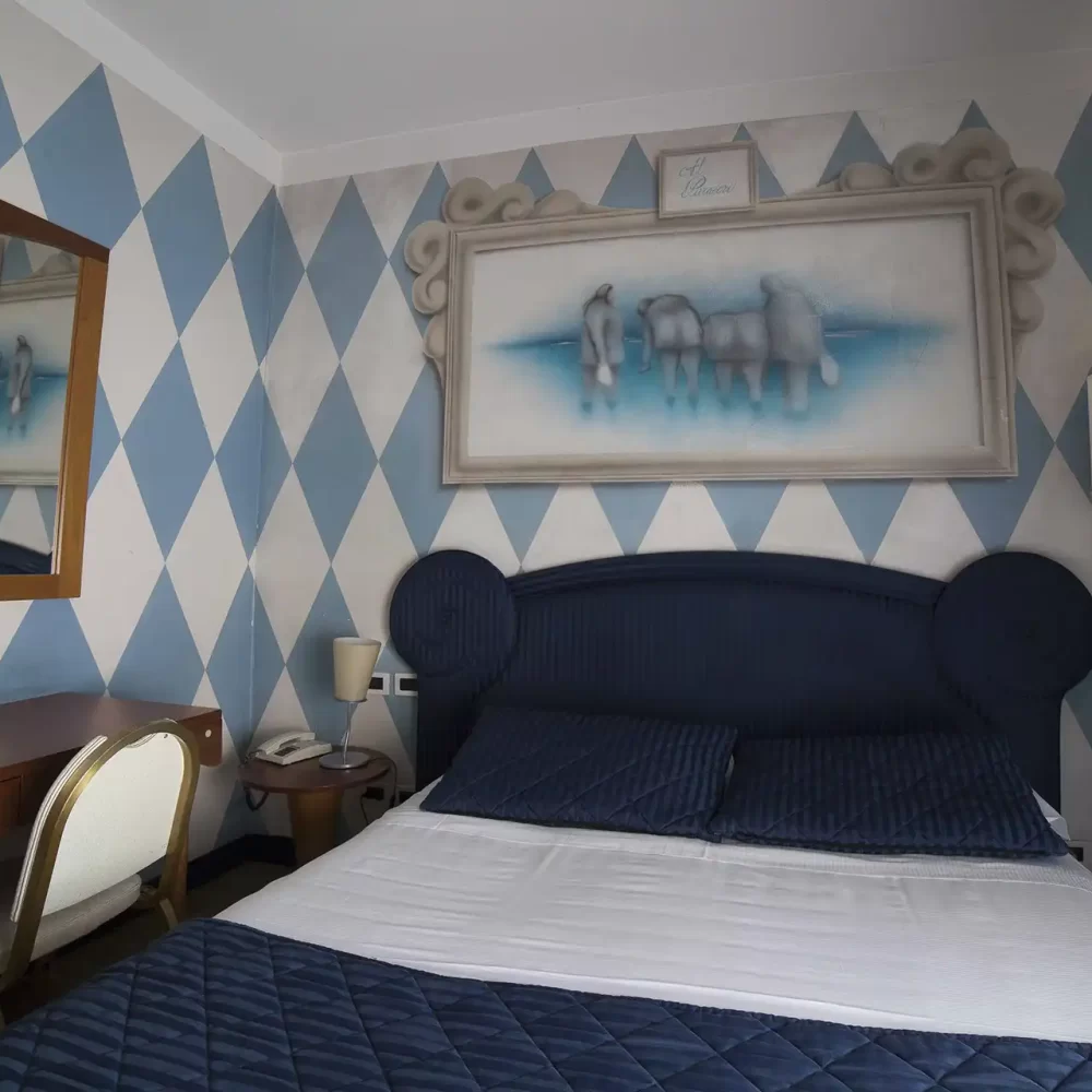 Camera da letto con letto matrimoniale, pareti a rombi blu, specchio e quadro.