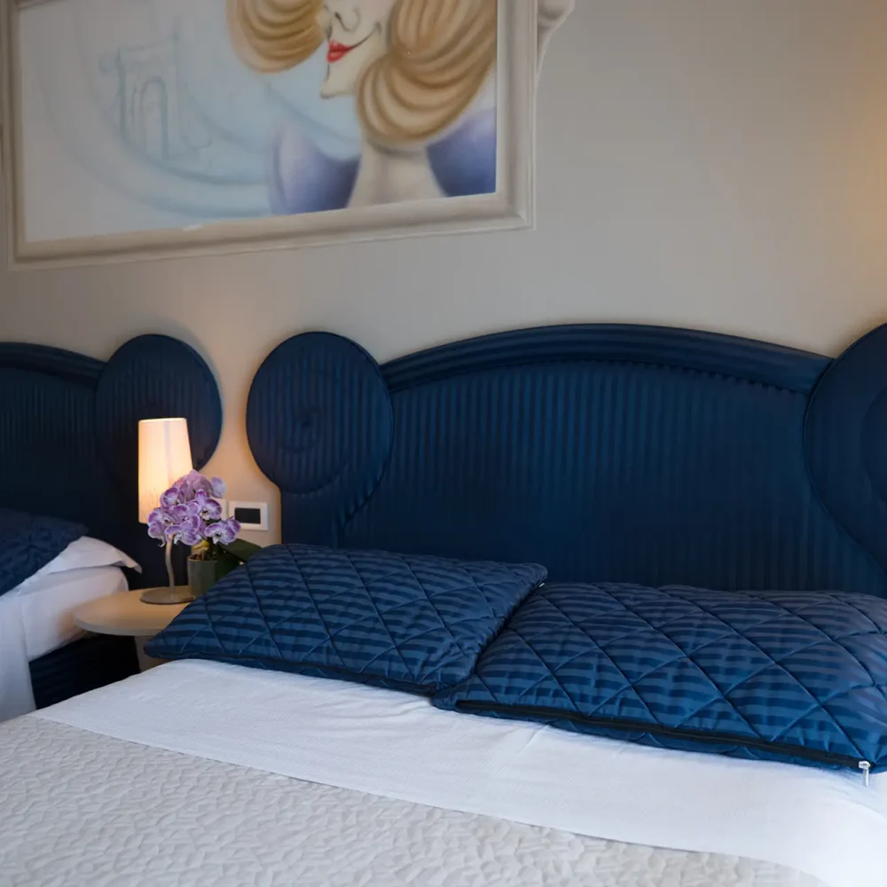 Due letti con testiere blu in una camera d'albergo ben illuminata.