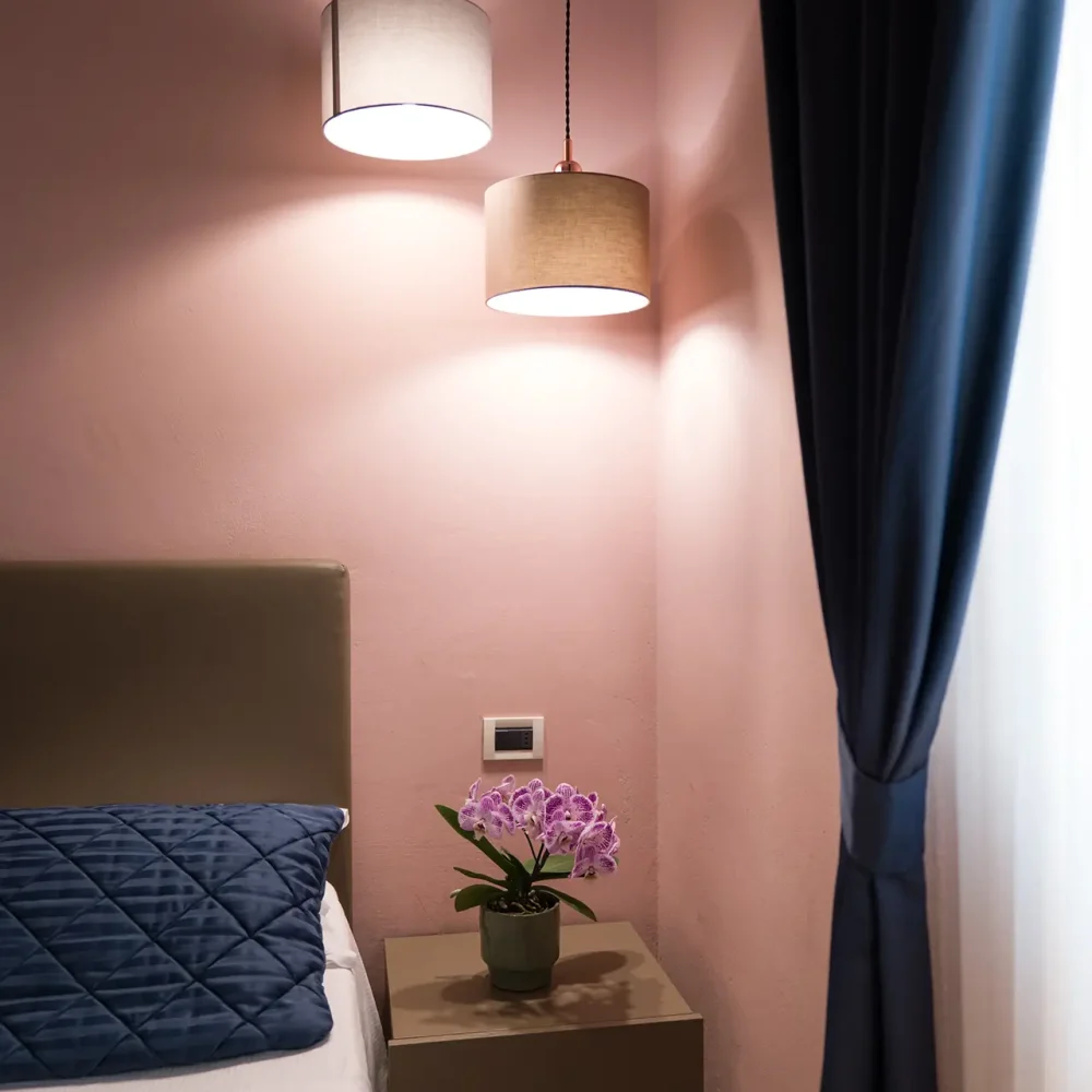 Camera da letto con pareti rosa, comodino con pianta di fiori e lampade a sospensione moderne.