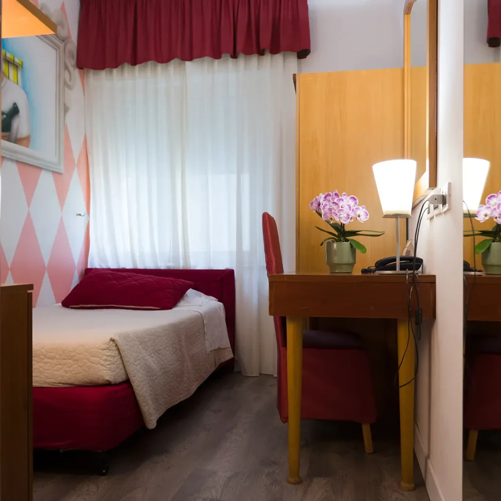 Camera d'albergo con letto singolo, scrivania e arredamento moderno.