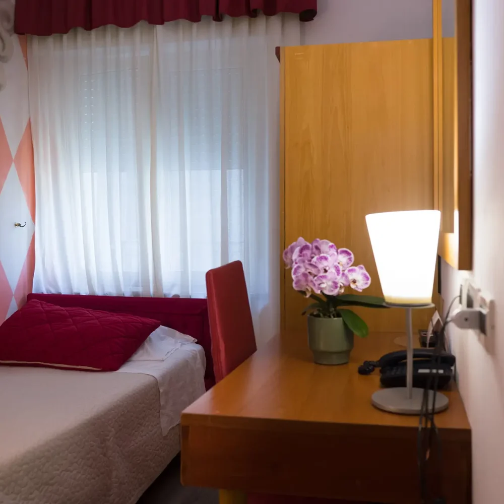 Una camera da letto con un letto singolo, specchio e scrivania decorata con fiori.