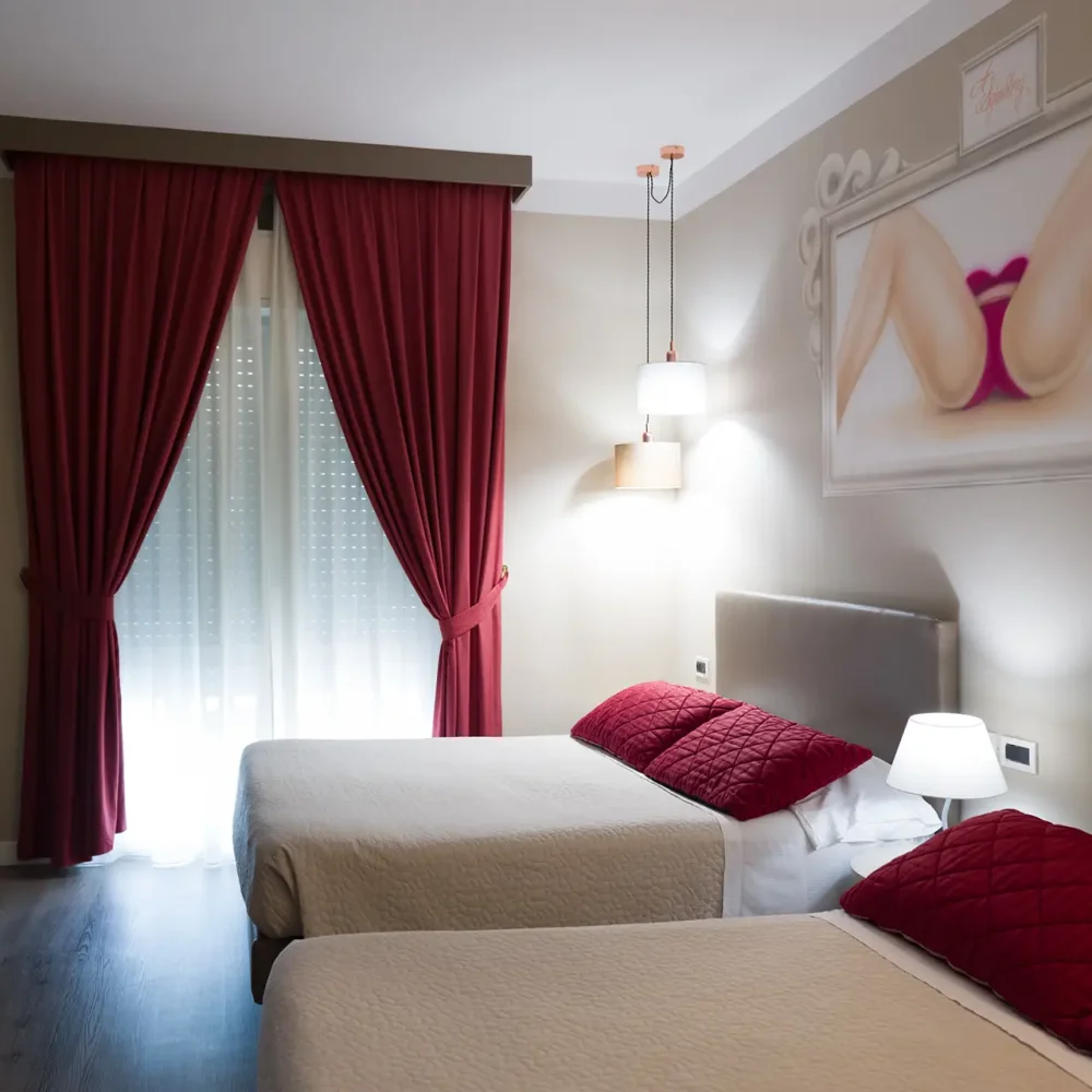 Camera d'albergo con due letti singoli e decorazioni dai toni rossi.