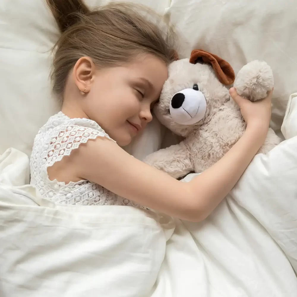 Bambina che dorme abbracciando un peluche a forma di cane nel letto.