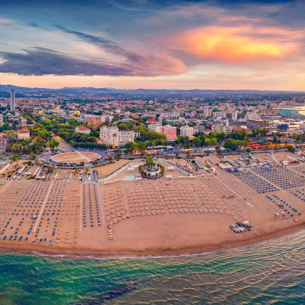Veduta panoramica di una spiaggia affollata al tramonto con una città sullo sfondo.