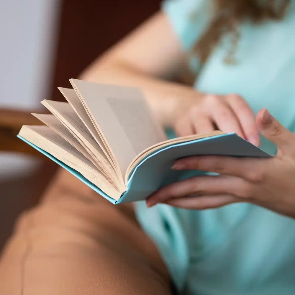 Persona che legge un libro tenuto con una mano.