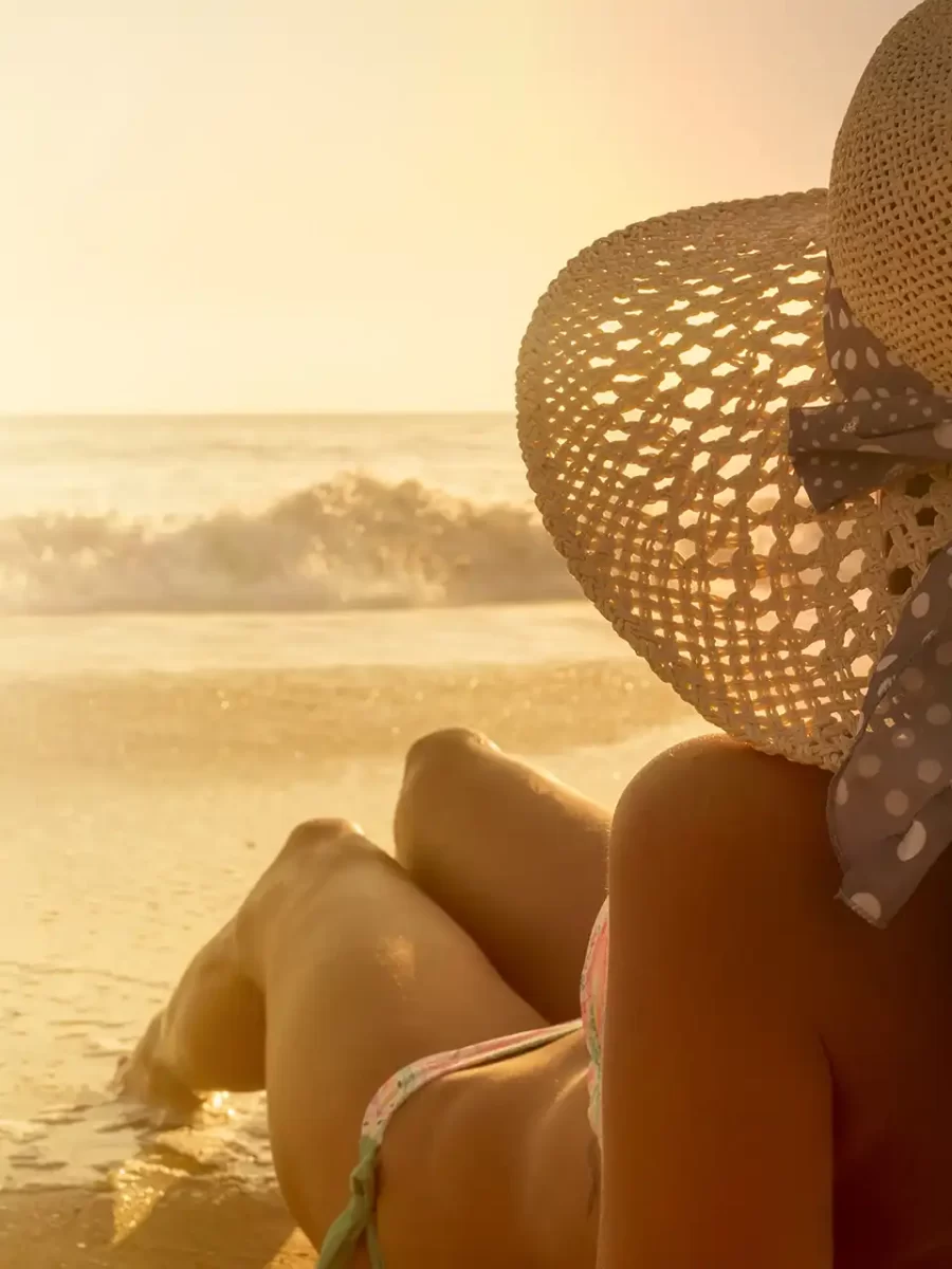 Donna sdraiata in spiaggia al tramonto con un cappello di paglia.