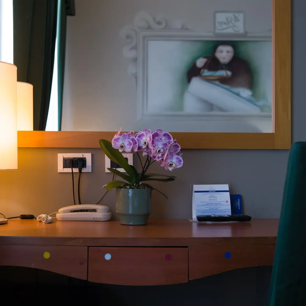 Tavolo da toeletta con lampada, orchidea e specchio riflettente una persona.